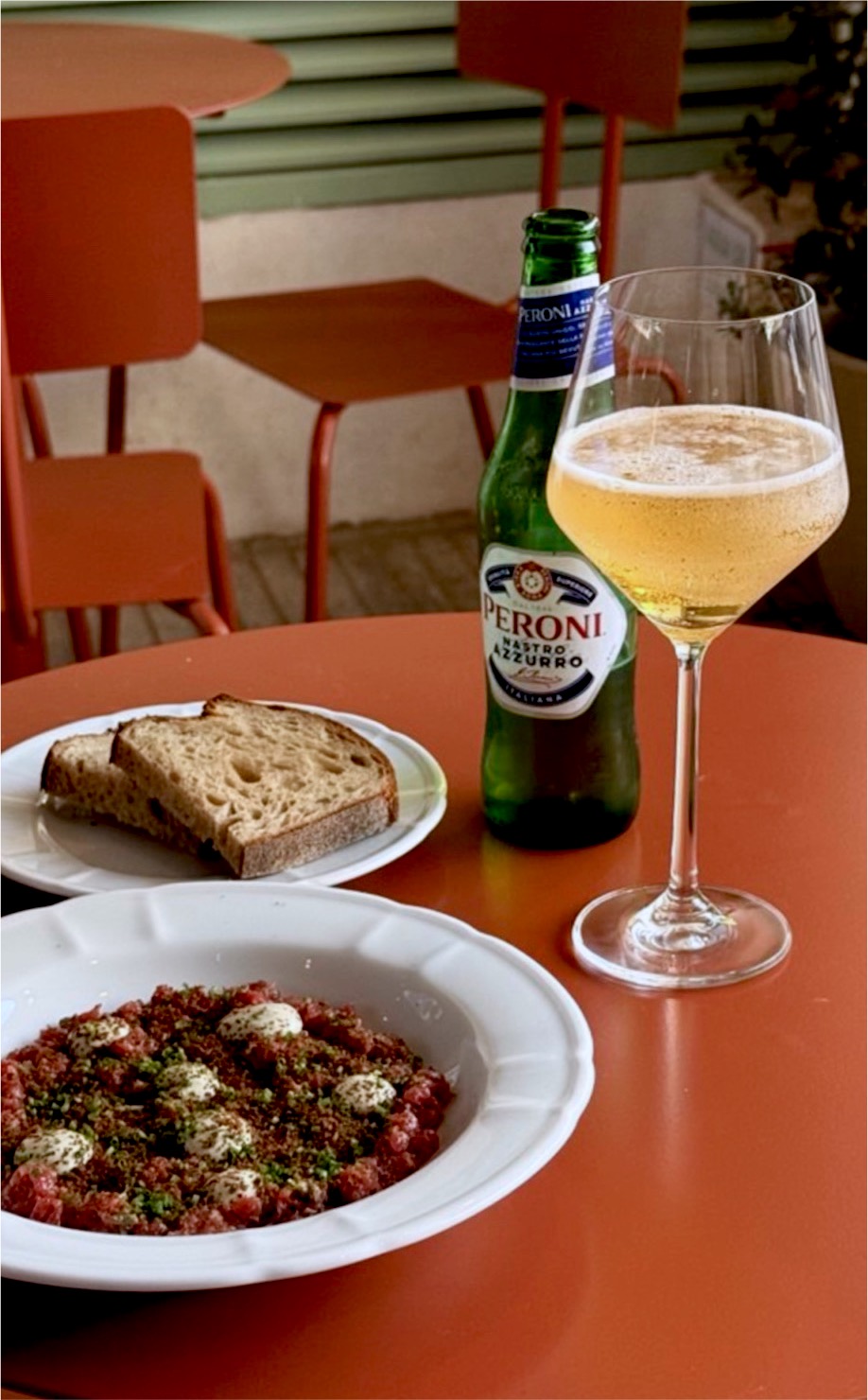 Tartar de carne, pan de masa madre, una Peroni y una copa sobre una mesa color terracota.