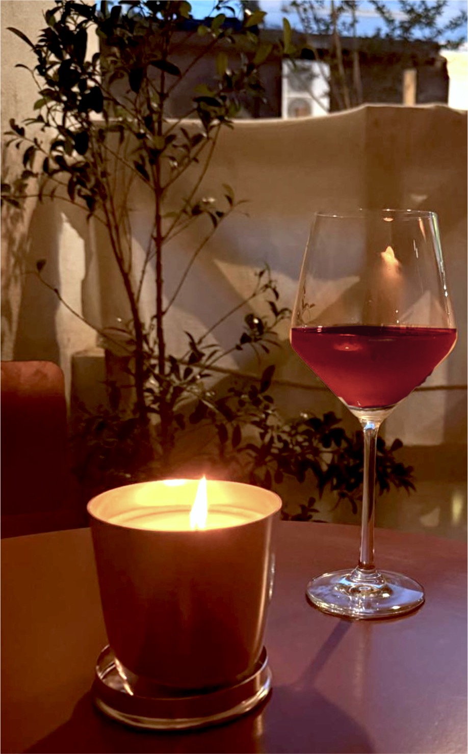 Una copa de vino tinto junto a una vela en la terraza, al atardecer.